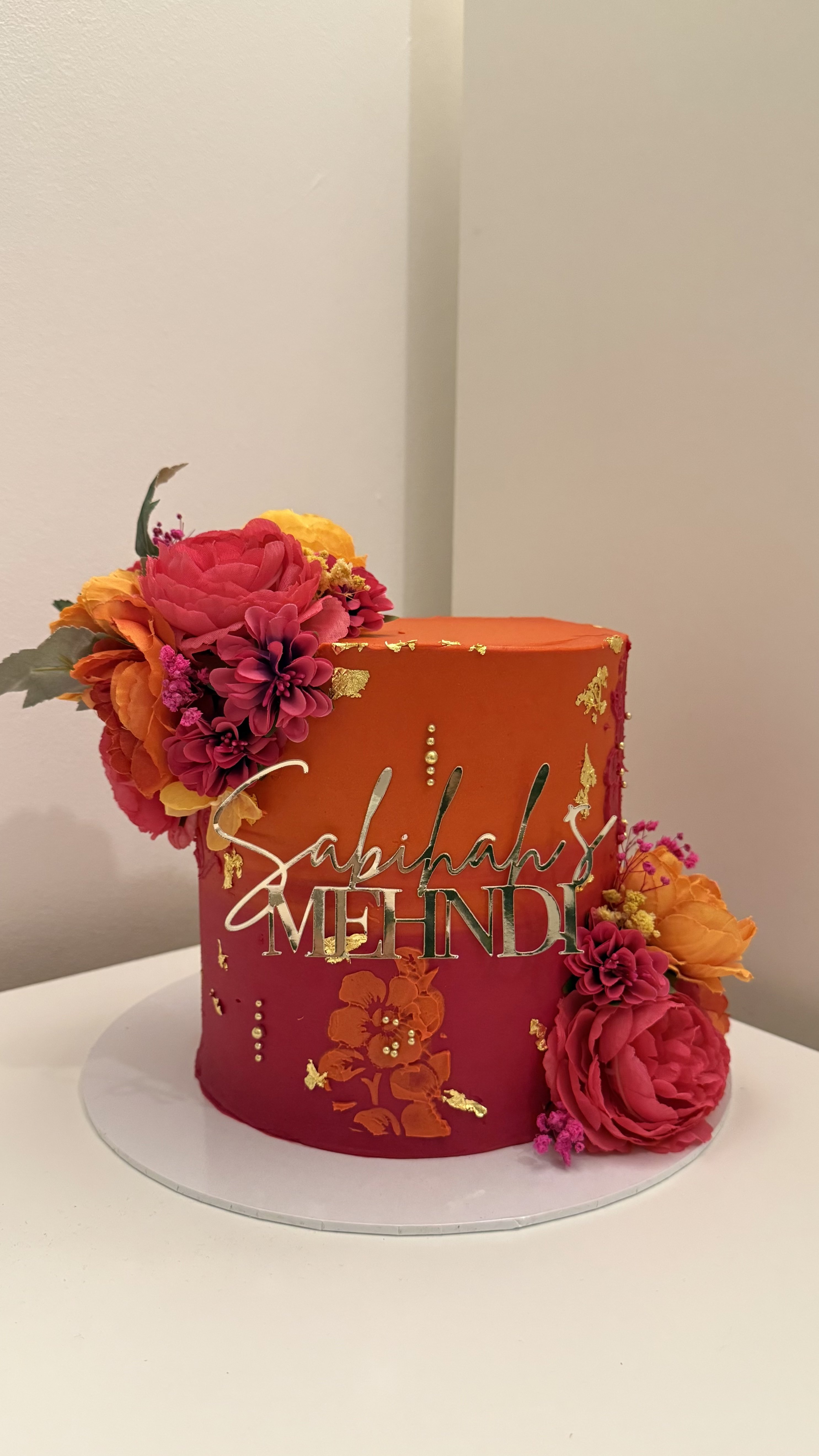 Mehndi cake with pink and orange ombré buttercream, flowers, and gold leaf